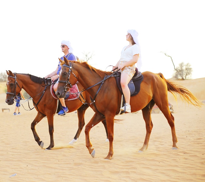 A young girl waving happily while riding a brown horse in the desert.