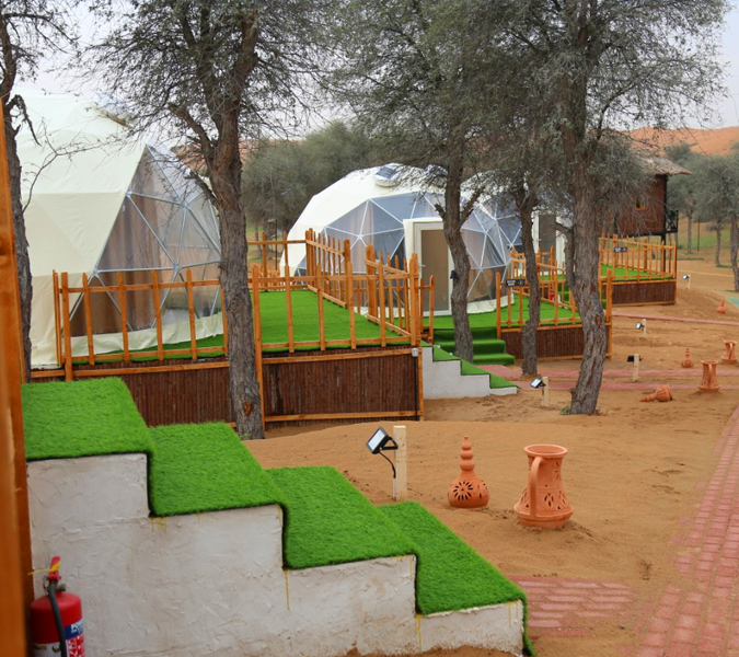 A group of geodesic dome tents in a desert camp, surrounded by trees and a landscaped walkway.