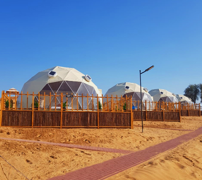 A row of large geodesic dome tents in a desert setting under a clear blue sky.