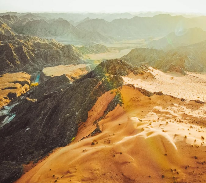 A striking aerial view of a desert mountain landscape with sunlit dunes.