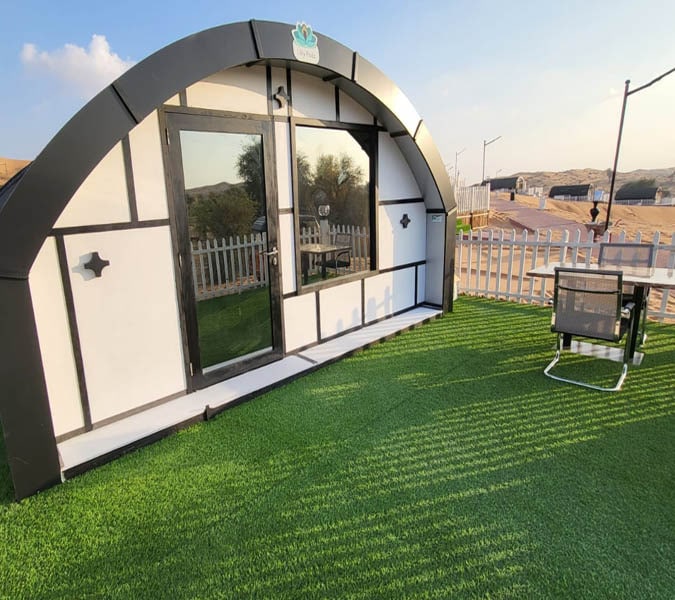 A modern dome tent with a green outdoor seating area in a desert campsite.