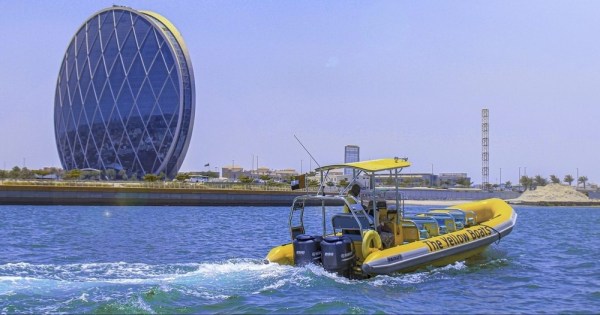 A bright yellow boat passing by the iconic circular Aldar HQ in Abu Dhabi.