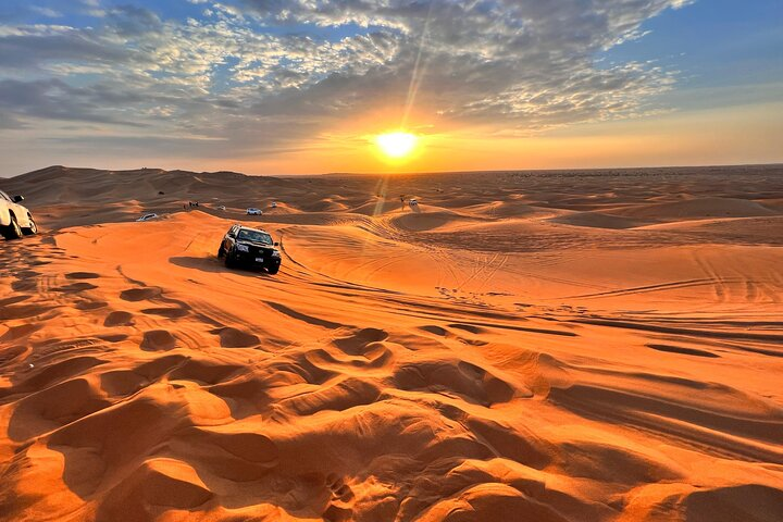 4x4 car driving on red sand dunes at sunset during Dubai desert safari