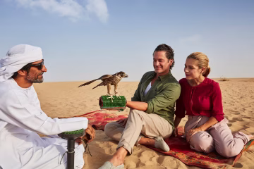 Couple enjoying falconry experience in Dubai desert with trained falcon perched on gloved hand
