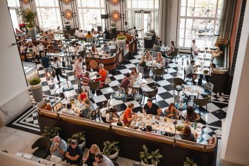 A high-angle view of a crowded, upscale restaurant with a black-and-white checkered floor and many people dining at various tables.