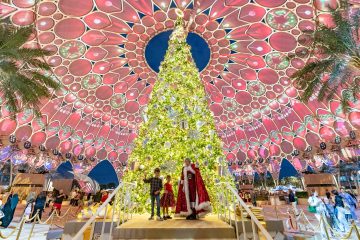 A giant, glowing Christmas tree standing under the intricate Al Wasl Plaza dome at Expo City with people walking nearby.